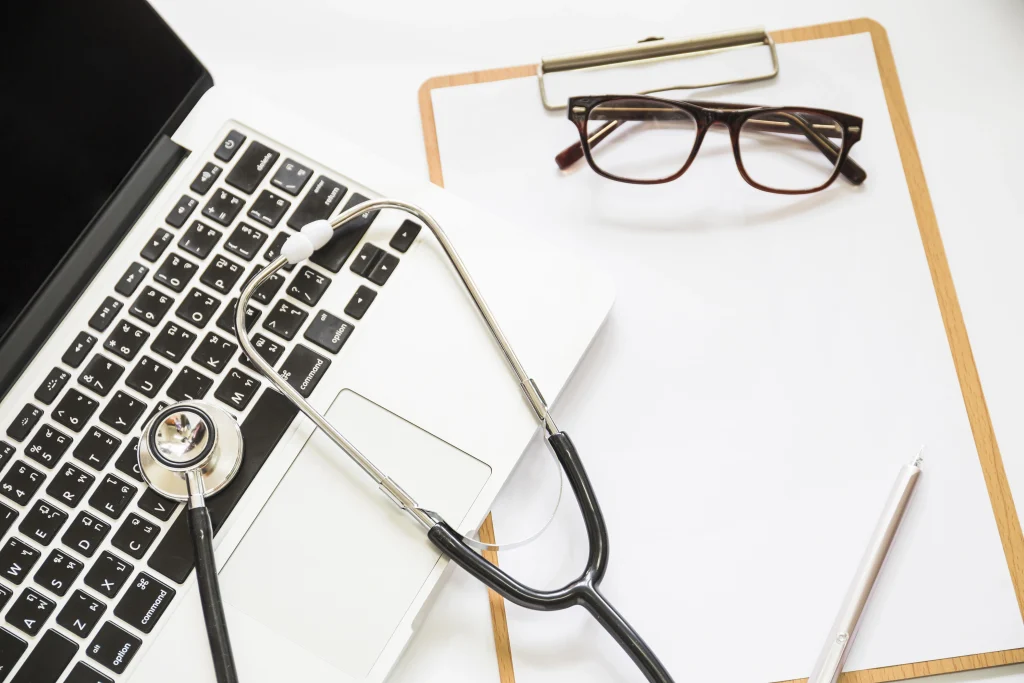 overhead view stethoscope open laptop with clipboard eyeglasses white background