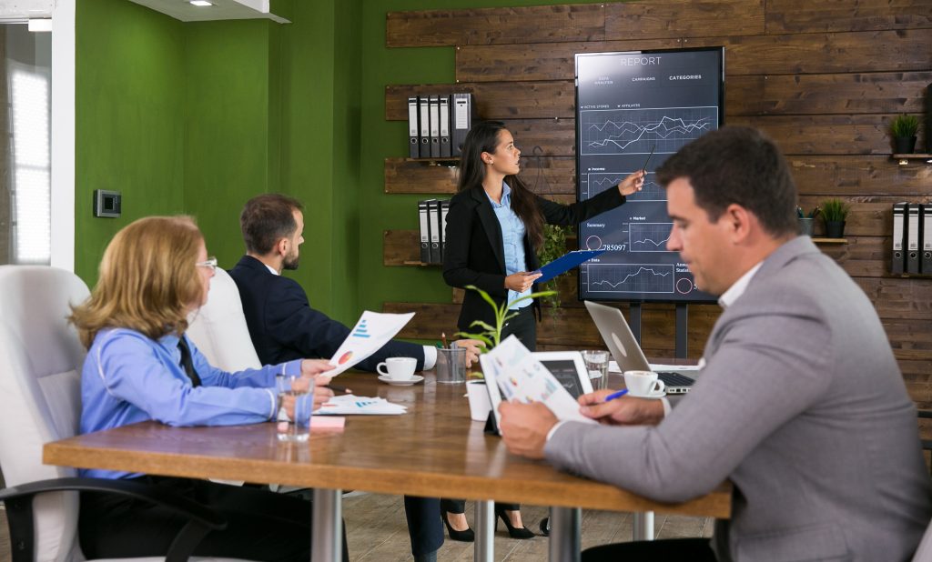 businessman in suit listening her colleague presenting charts on tv screen